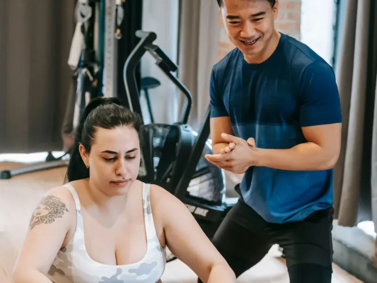Personal trainer in a t-shirt coaching a client at the gym